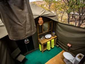 The open air en-suite bathrooms, with all the required amenities, including a flush toilet, bucket shower, lighting, basin and mirror.