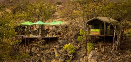 The main area deck and a room from across the dry riverbed, nestled in the Mopane grove.