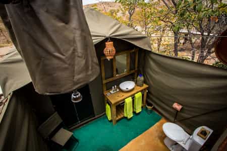 The open air en-suite bathrooms, with all the required amenities, including a flush toilet, bucket shower, lighting, basin and mirror.